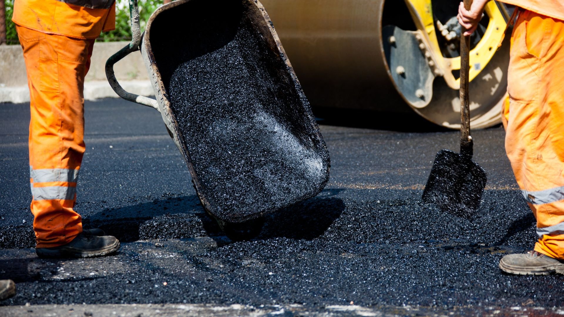 Workers laying hot asphalt with shovel and roller during road construction