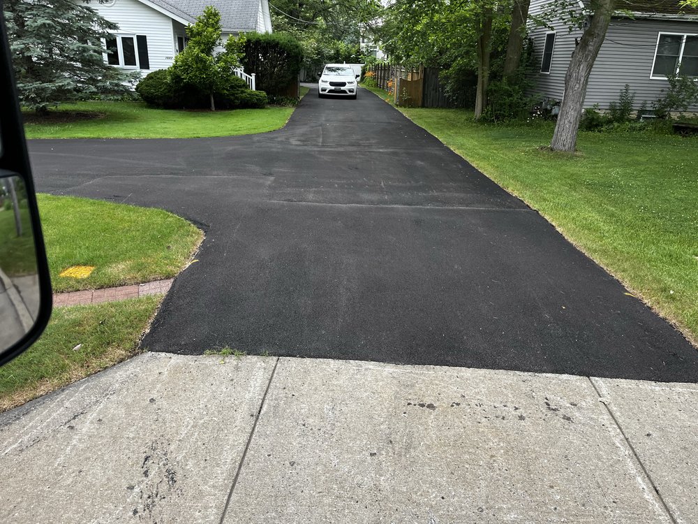 Newly paved black asphalt driveway between green lawns and suburban houses