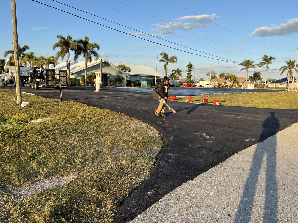 Worker sealing new asphalt driveway with palm trees in background