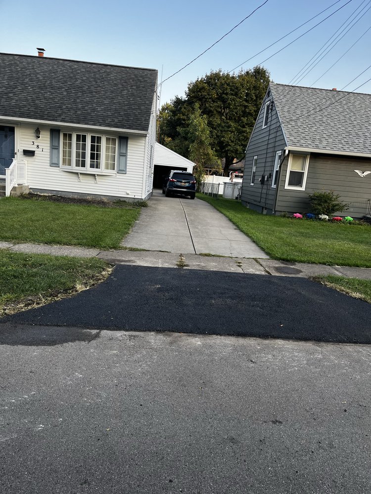 Two suburban houses with a driveway and recently sealed asphalt patch