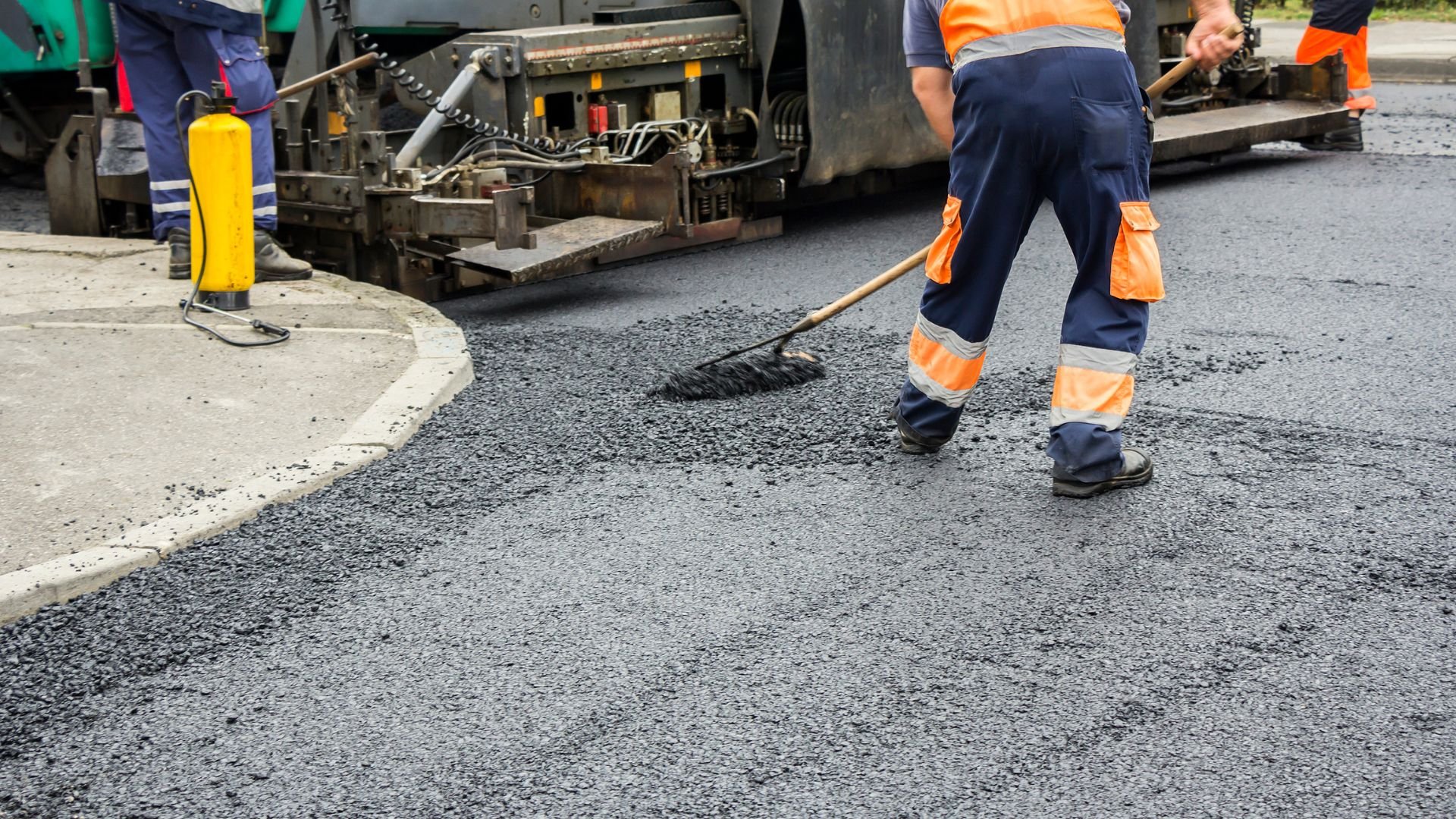 Road workers laying fresh asphalt with paving machine and broom
