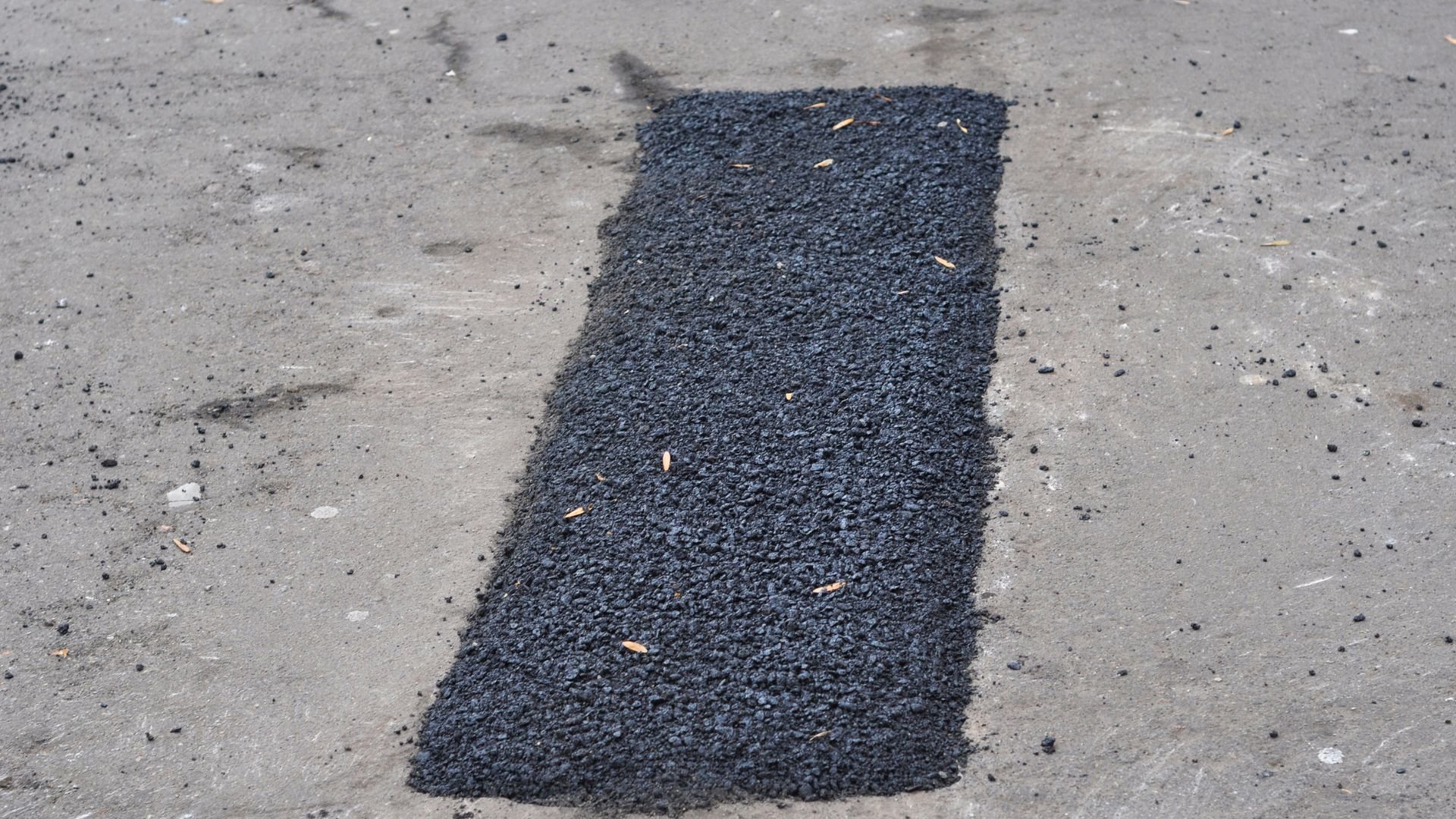 Fresh black asphalt patch on concrete surface with scattered debris