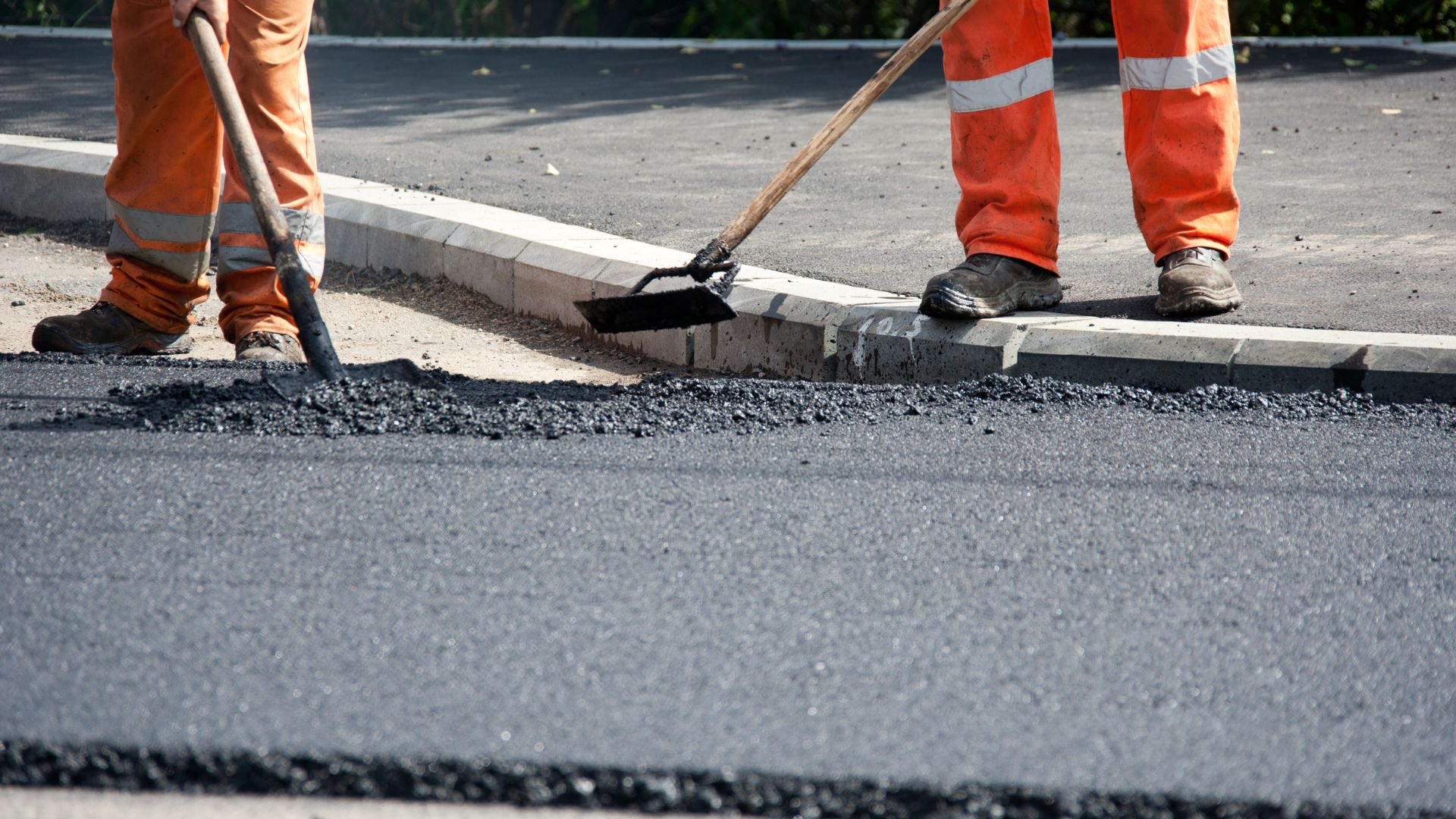 Road workers in orange uniforms smoothing fresh asphalt with tools
