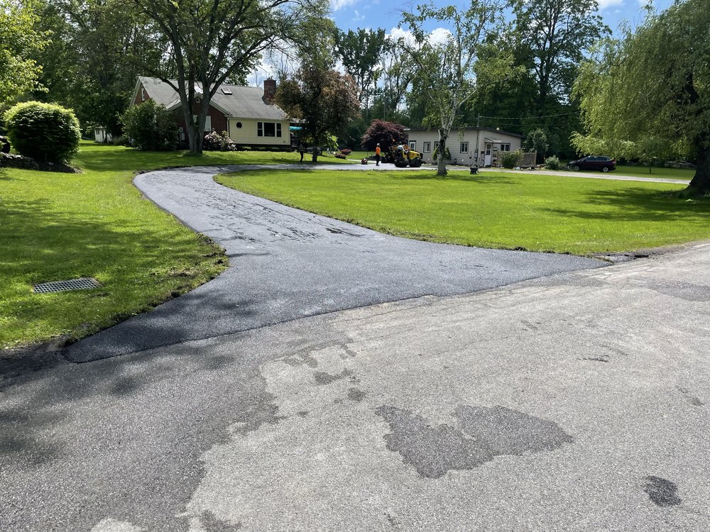 Curved asphalt driveway leading to suburban houses with green lawn