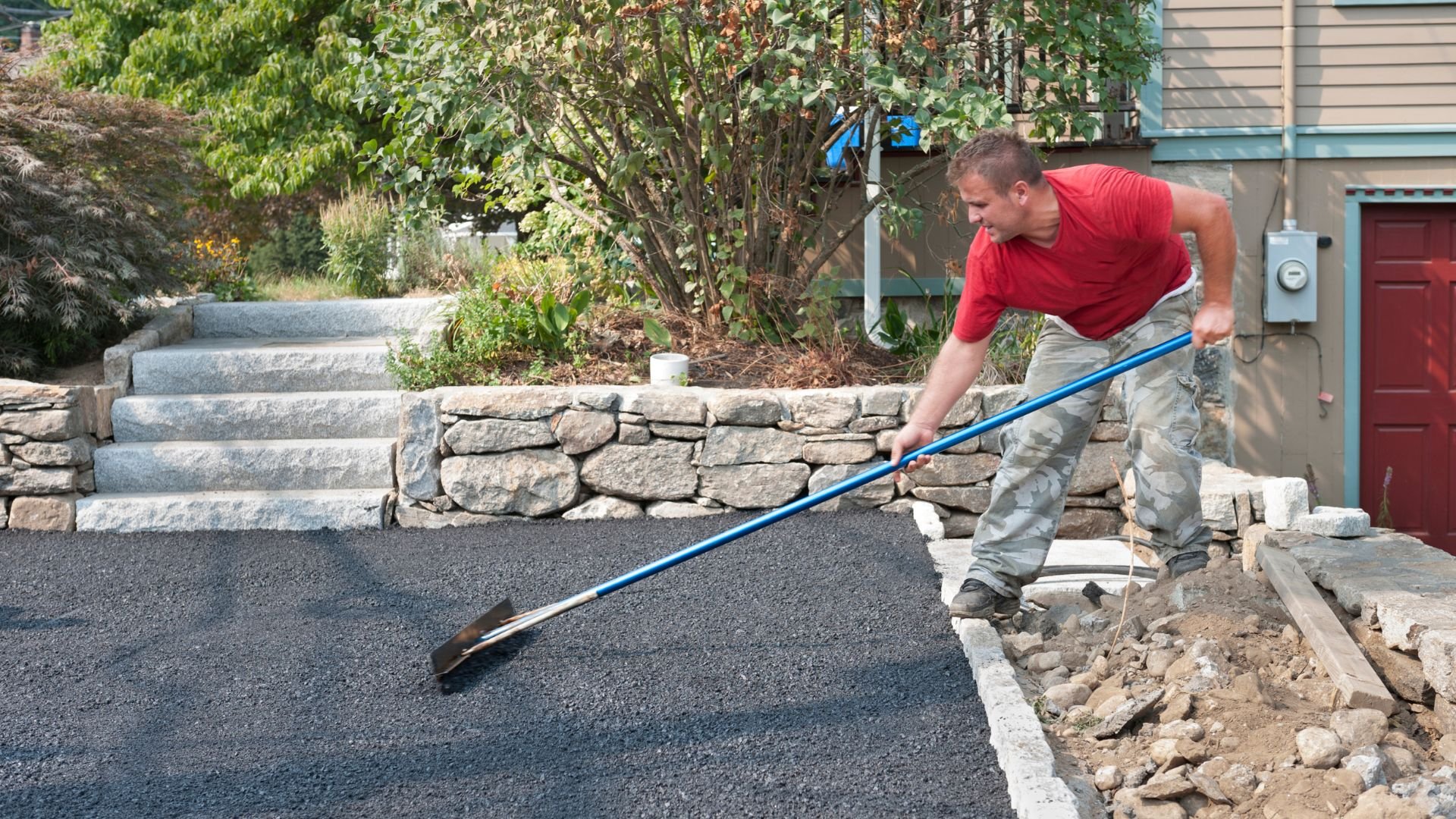 Worker smoothing newly laid asphalt driveway with long-handled squeegee