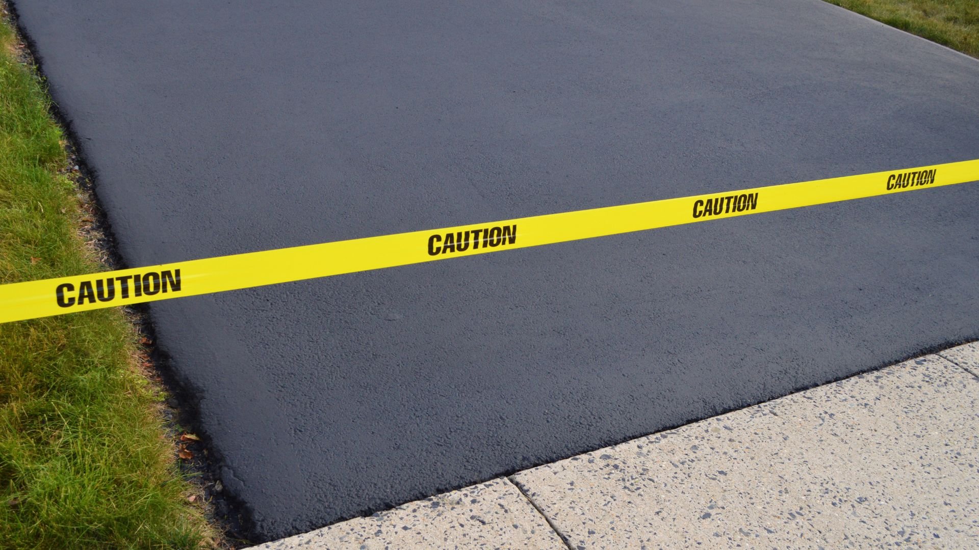 Yellow caution tape stretched across a newly paved dark asphalt surface