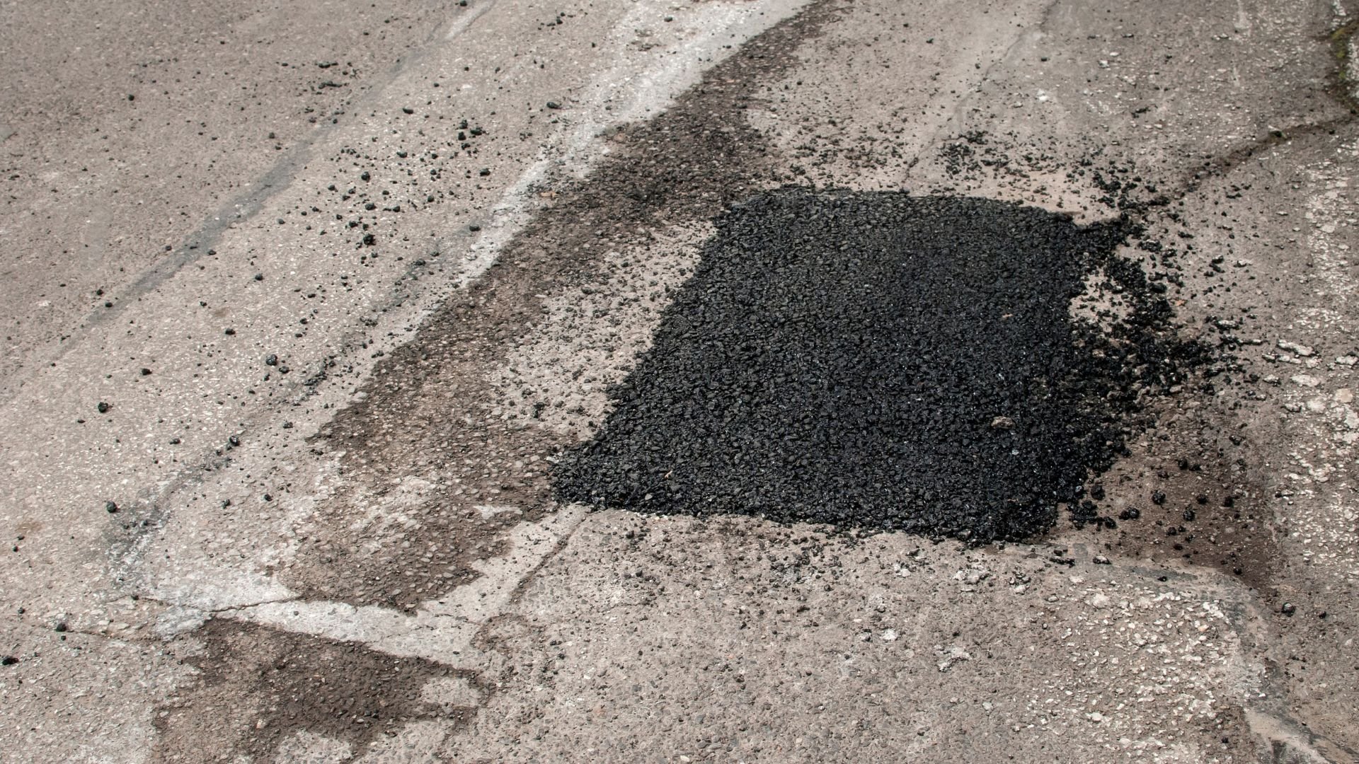 Fresh asphalt patch on damaged concrete road with scattered gravel