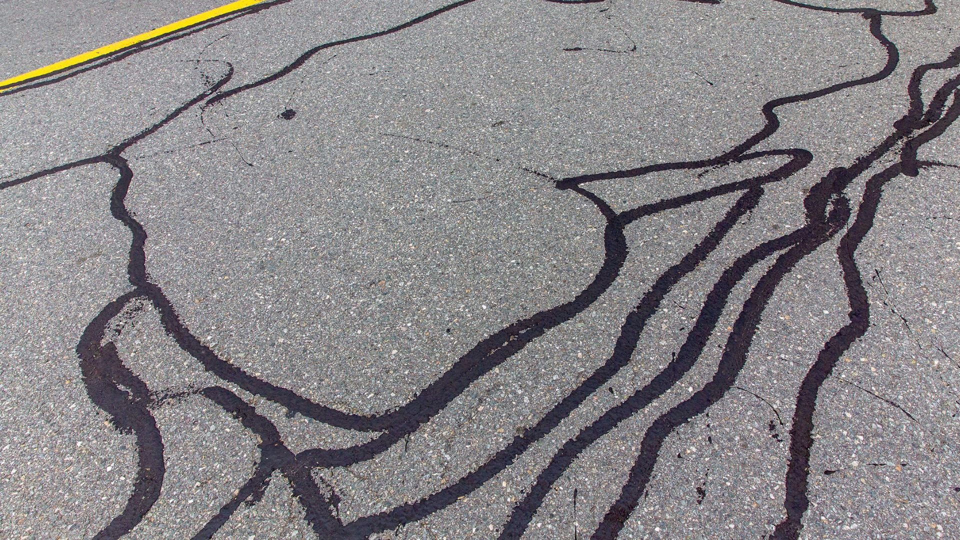 Cracked asphalt road with black fissures and a yellow line