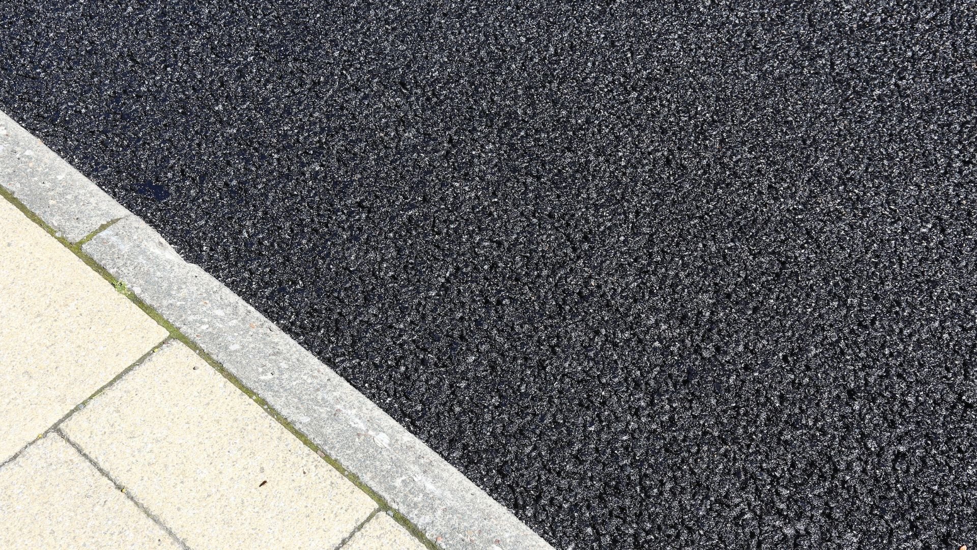 Asphalt road meets light concrete sidewalk at an angular diagonal